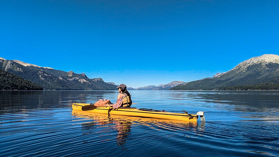 A kayaker gliding across a serene Patagonian lake surrounded by mountains