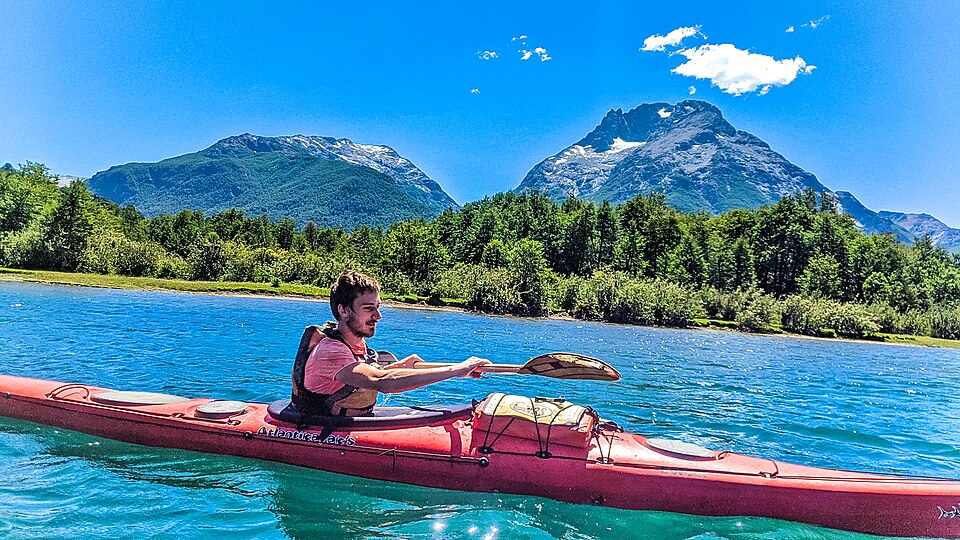 A man kayaking on a calm lake with Patagonian peaks in the distance