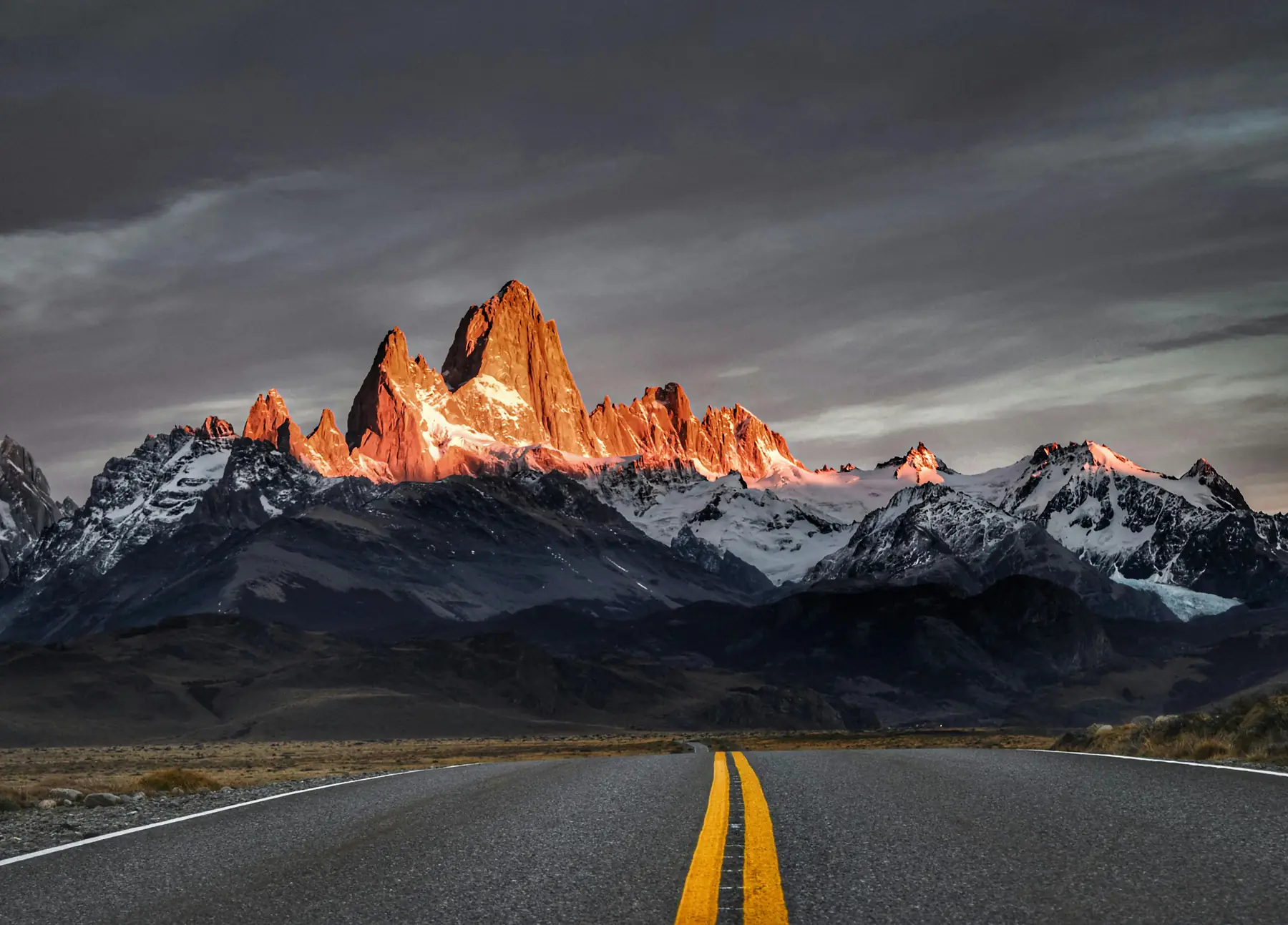 A long-distance bus traveling along a straight road through the vast Patagonian steppe