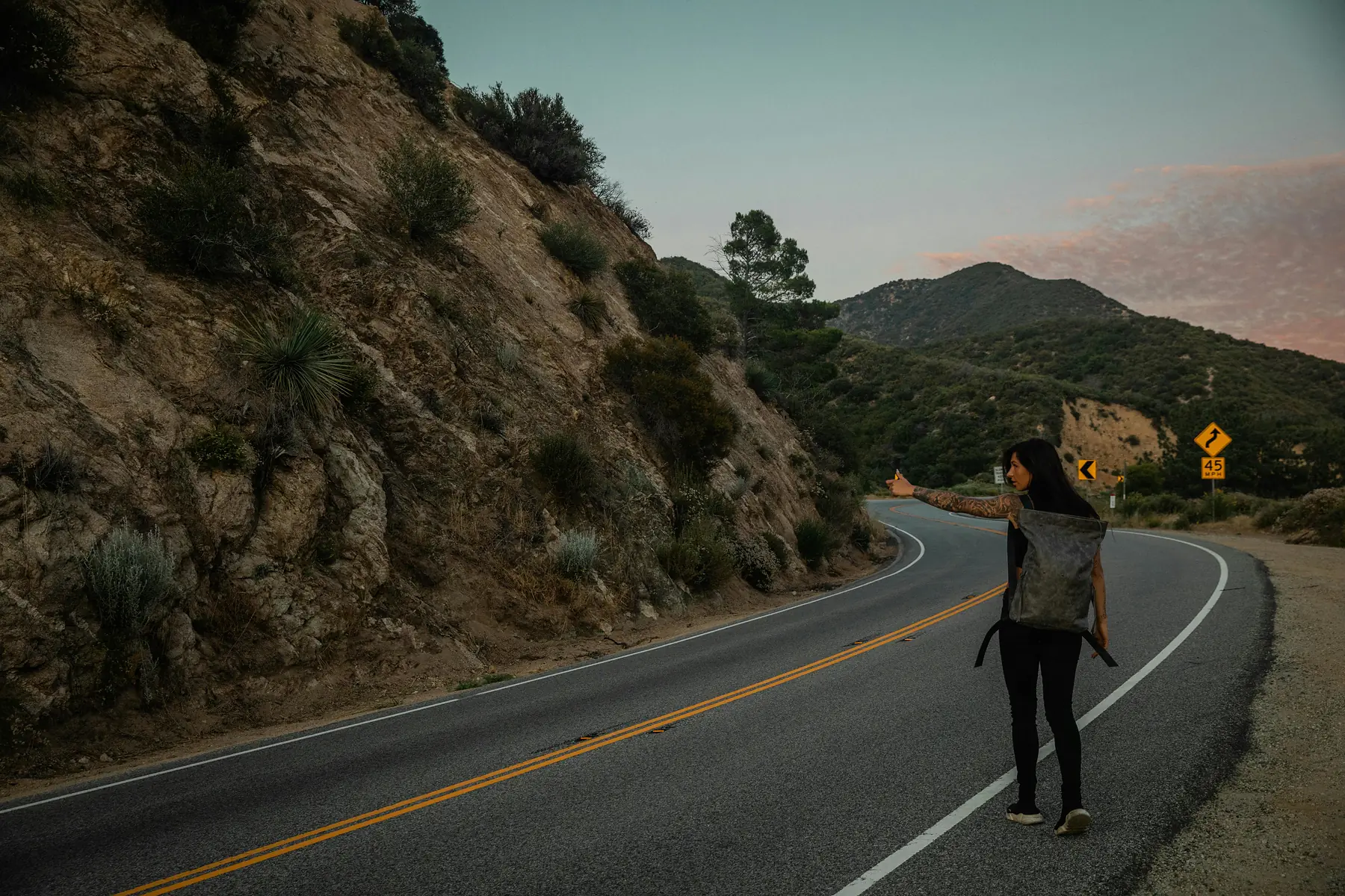 A backpacker hitchhiking along a remote Patagonian road with mountains in the distance
